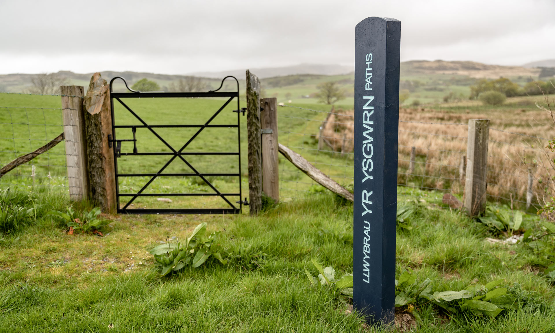 A signpost with 'Yr Ysgwrn Paths' stands by a gate that leads onto Yr Ysgwrn's walking paths