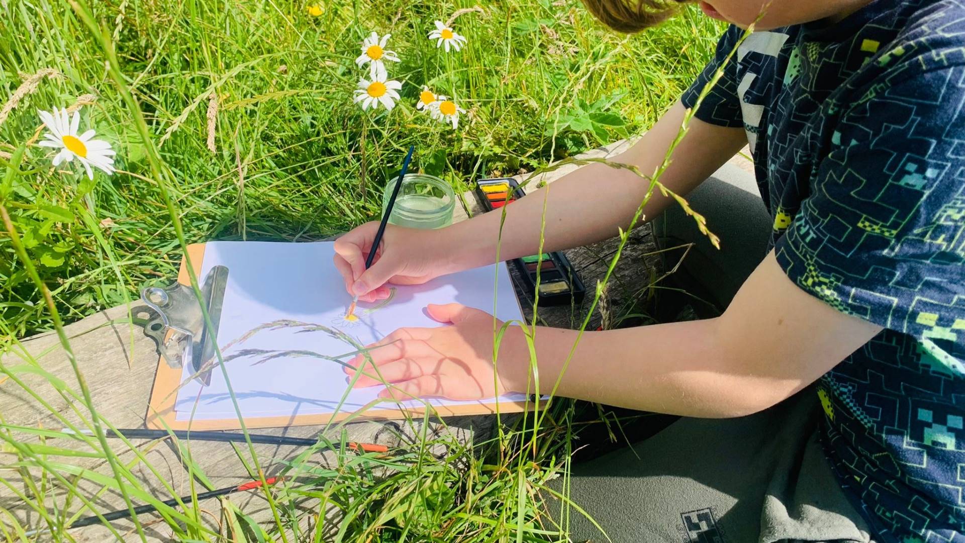 A child draws a flower in a meadow.