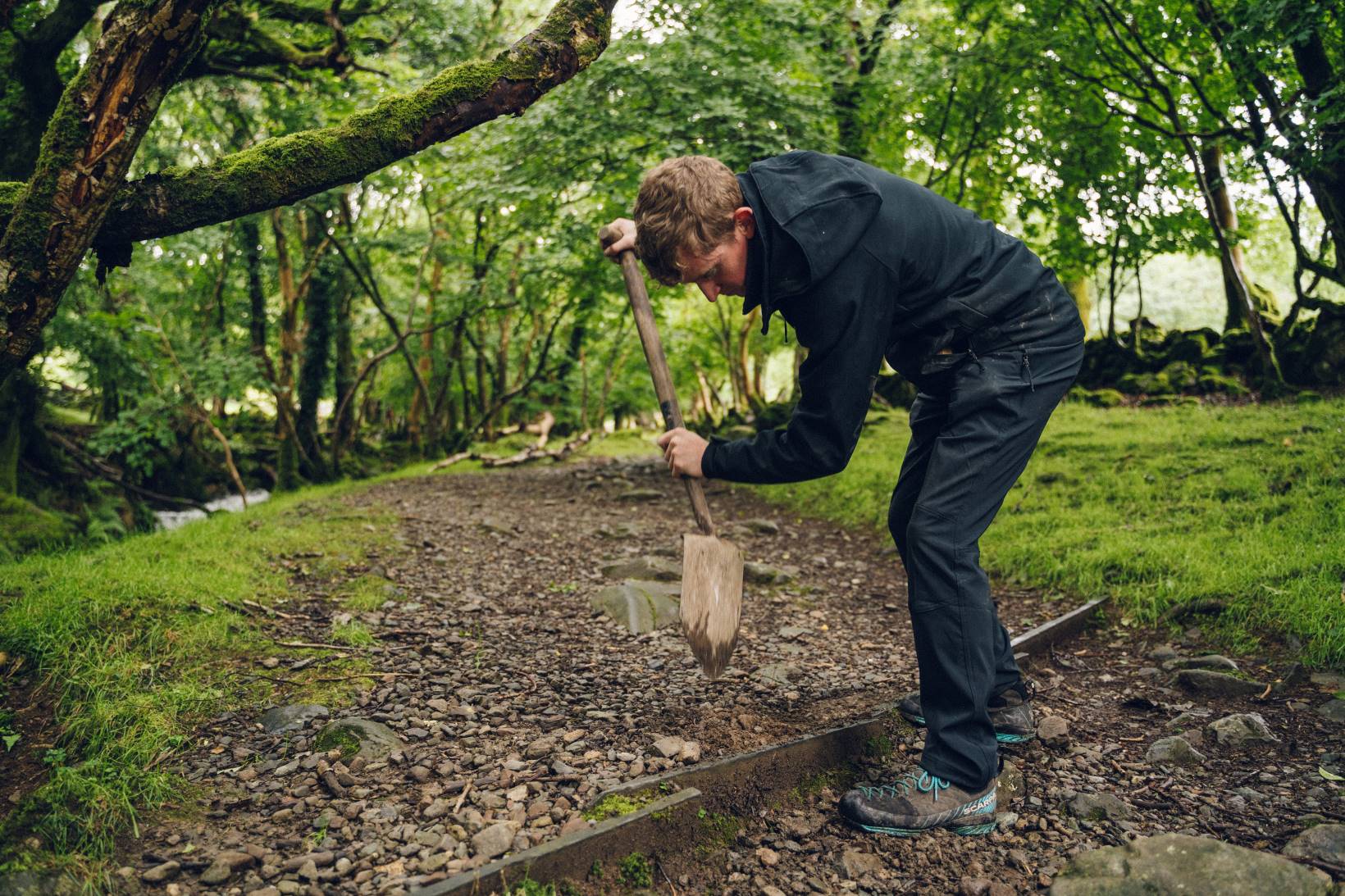 A National Park Authority warden uses a spade to work an a woodland footpath.